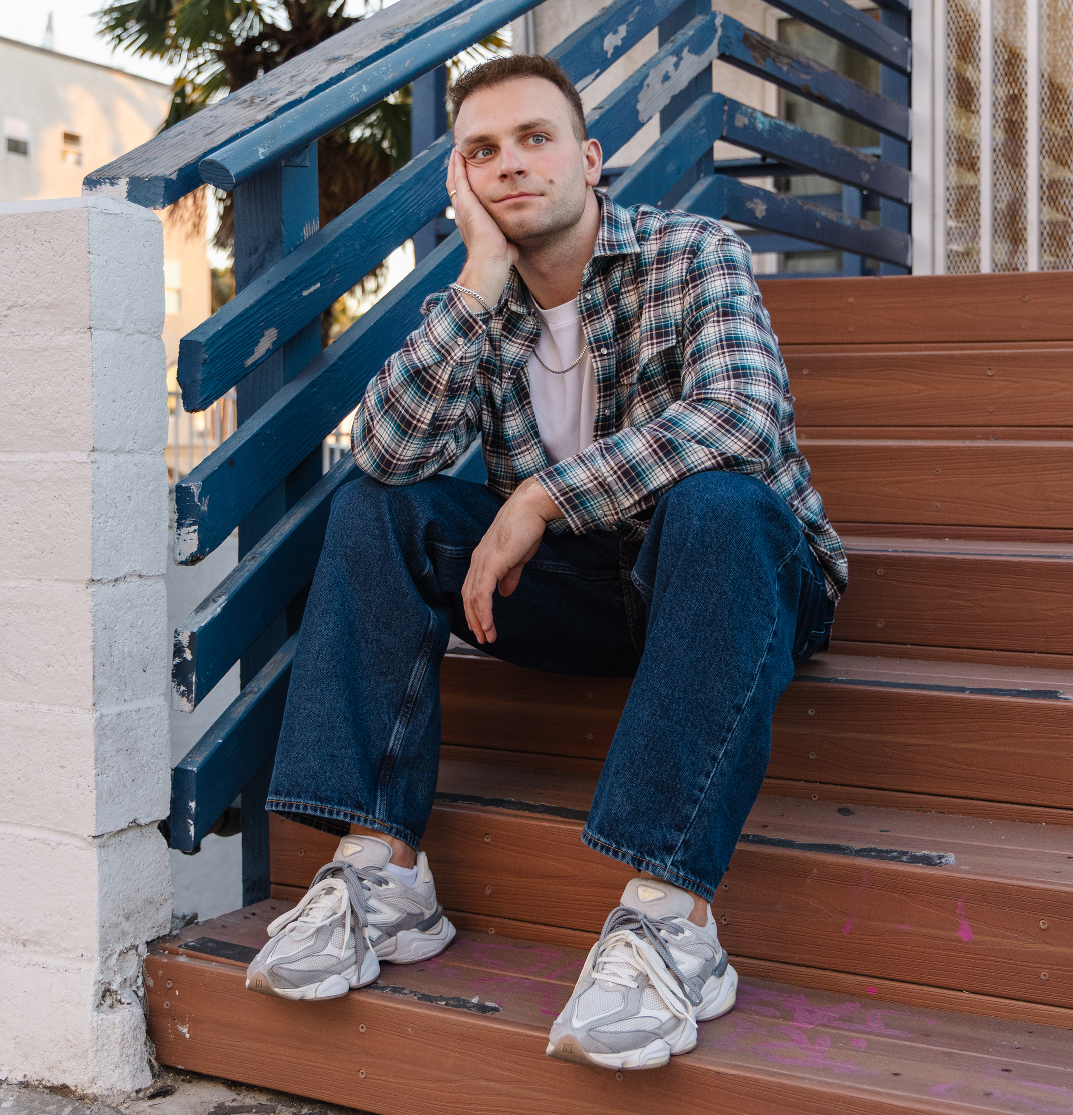 Man sitting on wooden steps wearing a plaid shirt and jeans.
